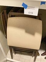 Stacked brown wood folding chairs with beige vinyl seats