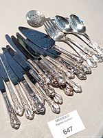 Group shot of silver-plated knives, spoons, servers with lot tag visible