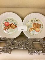 Front view of both pie plates showing apple and peach designs with trivet below