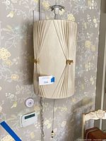 Full view of wall sconce mounted on wall, showing drum shade, mount and pull chain