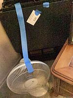 white pedestal floor fan and stacked black folding trays in corner
