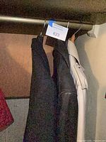 Two dark coats and one white coat hanging on closet rod
