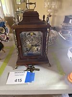 Front view of WUBA wood mantel clock showing dial, moonphase, brass accents, glass door, winding keys on table