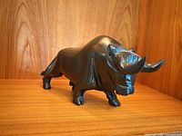 Front three-quarter view of carved black stone rhinoceros on wooden shelf