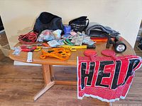 All items laid on table including jumper cables, tow strap, flashlight, reflectors, food and water packets, blanket, HELP sign