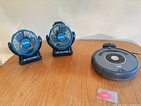 Lot overview showing two Makita fans, Roomba vacuum, charging dock and cleaning tool on tabletop