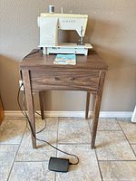 Singer sewing machine on wood table with foot pedal visible