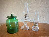 Front view of green glass jar with lid beside two clear glass oil lamps
