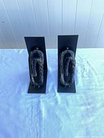 Front view of both black metal bookends displaying textured oval scroll accents and wear