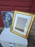 Gilt frame with mat shown next to acrylic sleeve for scale
