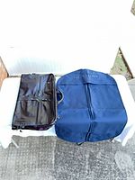 Both garment bags laid flat on table, navy cover and black travel bag visible