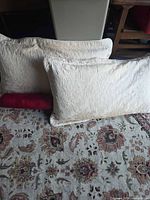 Two cream jacquard lumbar pillows in front of patterned rug with one pink bolster visible