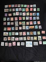 Full group view of 90 assorted mid-20th-century international stamps laid out on black background