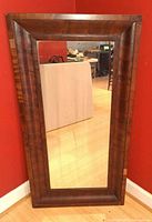 Full view of rectangular wood framed mirror standing against wall