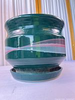Front view of dark green stoneware planter with pink/light gray stripe sitting on saucer