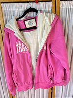 Front view of pink Exist zip hoodie showing hood, pockets, sherpa lining