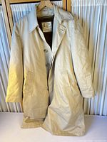 Full view of beige London Fog trench coat hanging, showing front, buttons, pockets, length