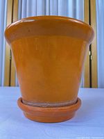 Front view of orange glazed ceramic flower pot on saucer