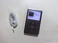 Front view of Apple iPod Classic 160GB displaying album art and click wheel, earphones coiled beside