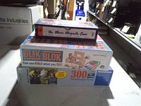 Three shrink-wrapped games stacked: The Movie Misquote Game, Blik Blok, Ravensburger 300-piece puzzle