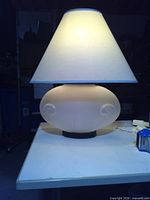 Front view of lit frosted glass lamp displaying body, base and shade