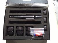Foam case interior showing microphone body, three mesh windscreen heads, three cylindrical accessories and small bag of rings