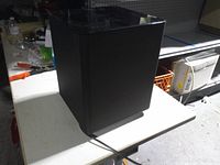 Full view of black Samsung subwoofer on table showing overall shape and attached power cord