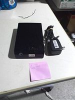 External hard drive front view beside power adapter and note indicating 2TB capacity