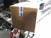 Sealed cardboard box with SMS tape and label identifying contents as universal shoe covers 100/pk
