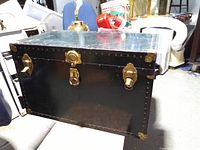Front view of black metal-clad trunk showing brass hardware and latches