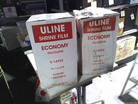 Front view of two Uline shrink film boxes showing product details and water damage