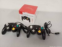 Front view of two black CIPON GameCube wired controllers with attached cables and retail box