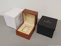 Wood watch box open showing interior and cushion, black outer box, white sleeve
