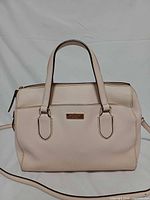 Front view of pale pink Kate Spade leather satchel with handles and logo plaque visible