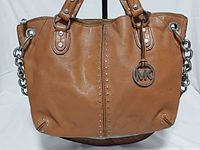 Front view of camel brown Michael Kors studded tote showing studs, handles, MK charm
