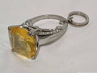 Side view showing yellow cushion-cut rhinestone, ring band with clear rhinestones, Juicy Couture engraving
