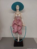 Front view of full sculpture showing figure with hat, metal rope, on black acrylic base