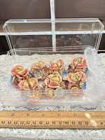 Eight floral porcelain place card holders in clear box with bubble wrap, ruler shows scale