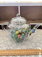 Front view of clear glass teapot with lid filled with multicolor marbles