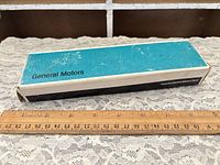 GM branded turquoise box top view beside ruler