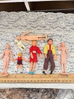 Overview of all seven dolls/figures on lace background with ruler for scale