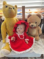 Group shot showing yellow teddy, tan teddy, red-dressed doll with ruler for scale