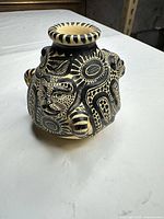 Front view of black ceramic vase showing figural faces and geometric motifs