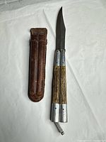 Knife folded out beside leather sheath on white background