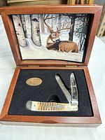 Open wooden display box showing knife, medallion, and deer artwork
