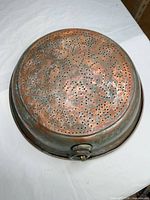 Top view of perforated copper colander showing patina and hole pattern