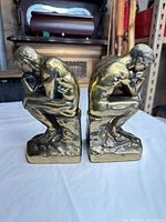 front side view of paired gold metal seated thinker bookends