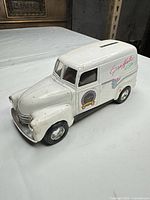 Full view of white metal panel van coin bank showing shape, roof slot, wheels, overall paint condition