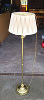 Full view of brass-tone floor lamp with pleated shade standing upright