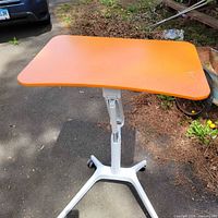 Full view of orange adjustable desk showing top and wheeled base